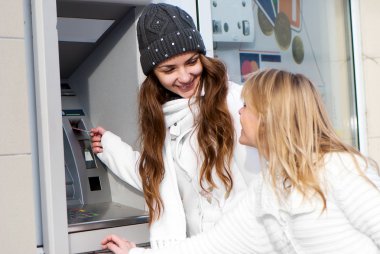 Happy girls withdrawing money from credit card at ATM clipart