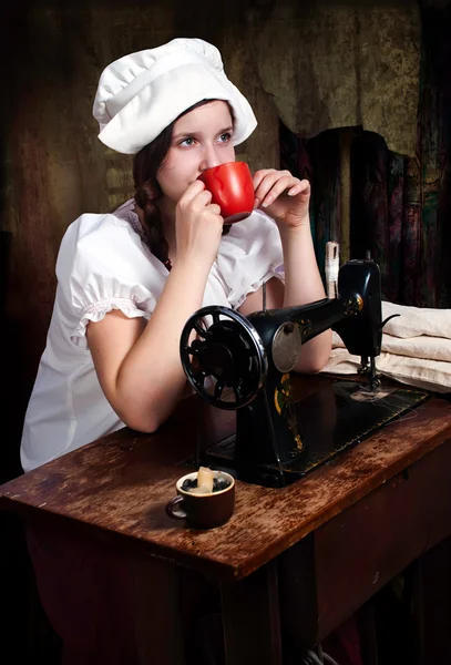 Porträt einer jungen Näherin mit rotem Becher neben alter Nähmaschine — Stockfoto