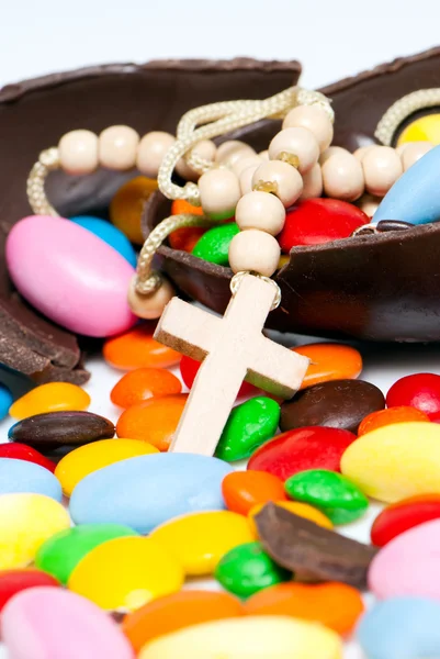 Kruis versleten op de hals tegen chocolade paaseieren en snoep — Stockfoto