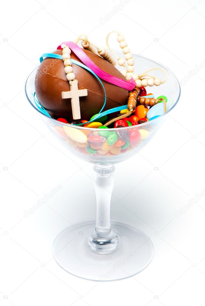Easter chocolate egg , sweets and cross in a glass on a light ba