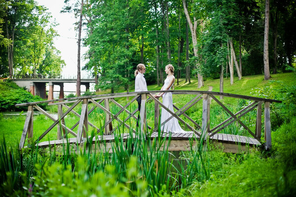 Bride and groom are standing on a bridge and holding their hands