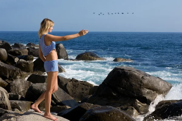 Aantrekkelijk meisje ontspannen op een rotsachtige strand door zee. — Stockfoto