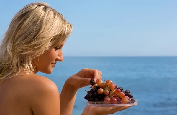Дівчина їсть виноград на пляжі біля моря . — стокове фото