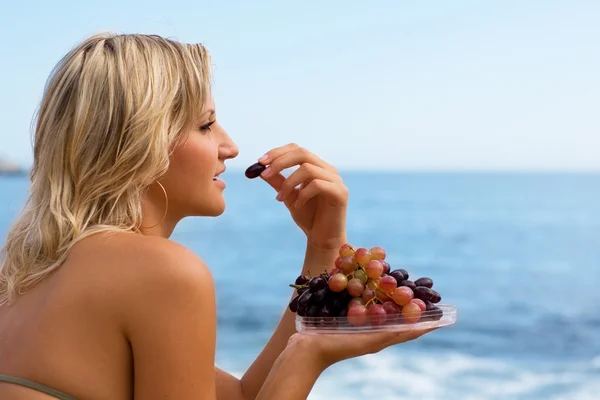 Meisje druiven eten op het strand door zee. — Stockfoto