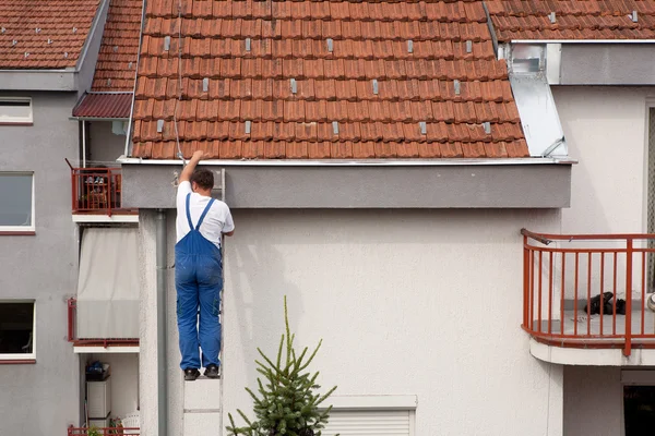 Человек на лестнице забирается на крышу — стоковое фото
