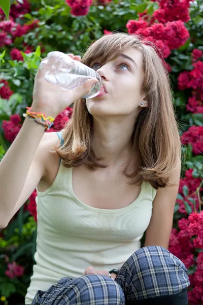 Adolescente chica beber agua de la botella en el jardín de flores —  Fotos de Stock