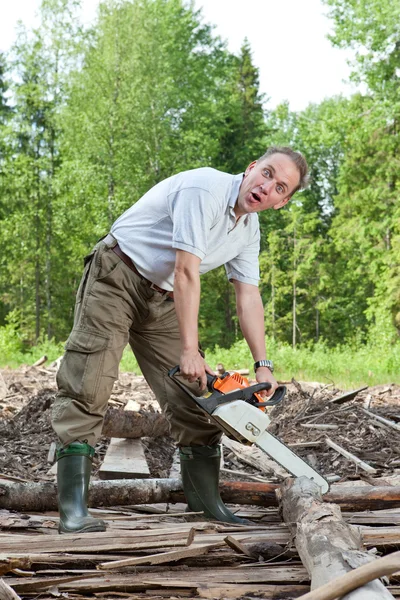 The surprised man with a chain saw in summer wood — Stock Photo, Image
