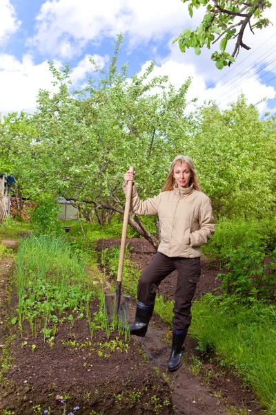 Die junge Frau gräbt an einem Sommertag ein Gartenbeet mit den ersten Sprossen aus — Stockfoto