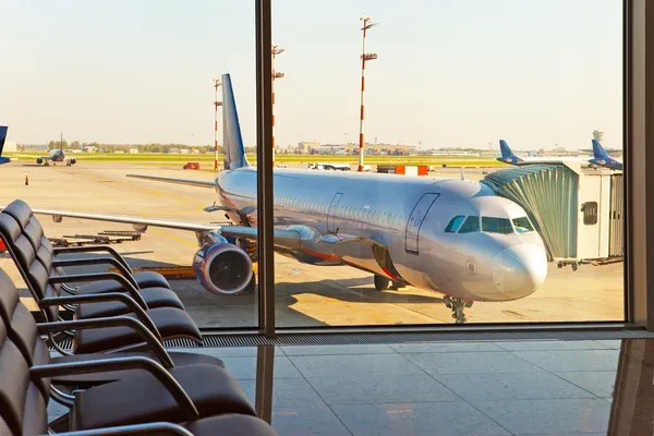 Sillones vacíos en la sala de espera del aeropuerto y avión detrás de la ventana — Foto de Stock
