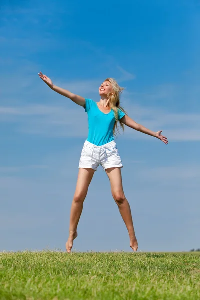 De gelukkige jonge vrouw springt in het veld — Stockfoto