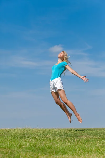 Die glückliche junge Frau springt auf das Feld Stockbild