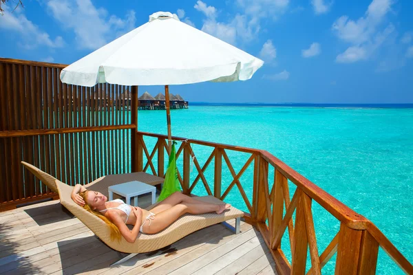 Mujer joven en el chaise lounge bajo la sombrilla cerca del mar.Maldivas . —  Fotos de Stock