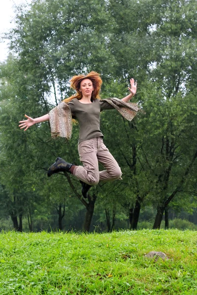 A menina pula em uma grama e árvores como um fundo — Fotografia de Stock