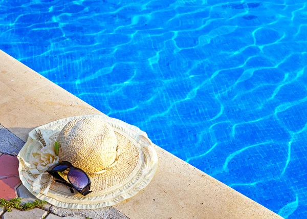 Солом'яний капелюх і сонцезахисні окуляри лежать поруч з басейном — стокове фото