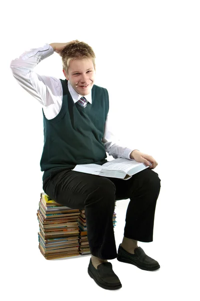 O estudante em um uniforme escolar senta-se em um pacote de livros — Fotografia de Stock