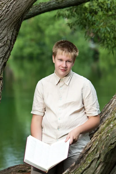 The young man with the book in park on the bank of lake — Stock Photo, Image