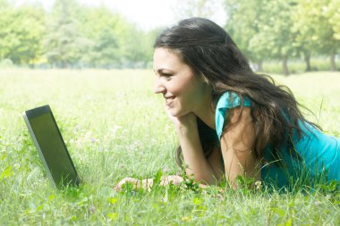 portre sevimli genç bir dişi bir lapt kullanarak parkta çim üzerinde yalan