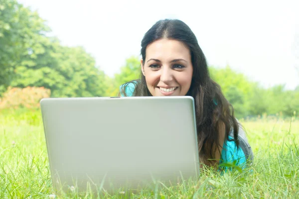 Porträt eines süßen Mädchens, das mit einem Laptop auf dem Rasen im Park liegt — Stockfoto