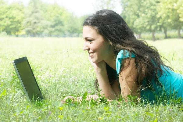 Portrét roztomilá mladá žena leží na trávě v parku pomocí lapt — Stock fotografie
