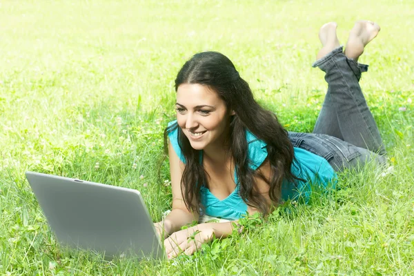 Retrato de una linda joven hembra acostada en la hierba del parque usando un lapt —  Fotos de Stock
