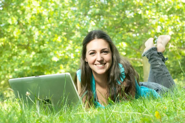 Portrait of a cute young female lying on the grass in the park using a lapt — Stock Photo, Image