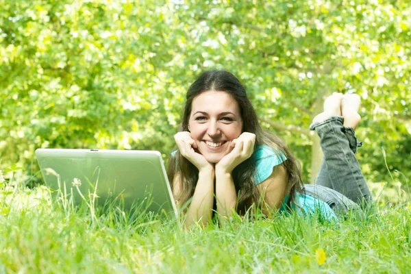Портрет милої молодої жінки, що лежить на траві в парку за допомогою ноутбука — стокове фото