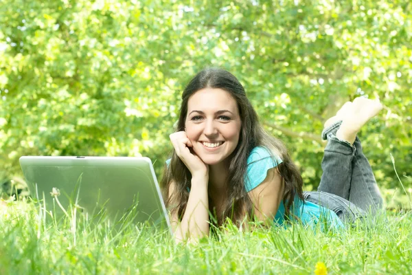 Retrato de uma linda jovem mulher deitada na grama no parque usando um lapt — Fotografia de Stock