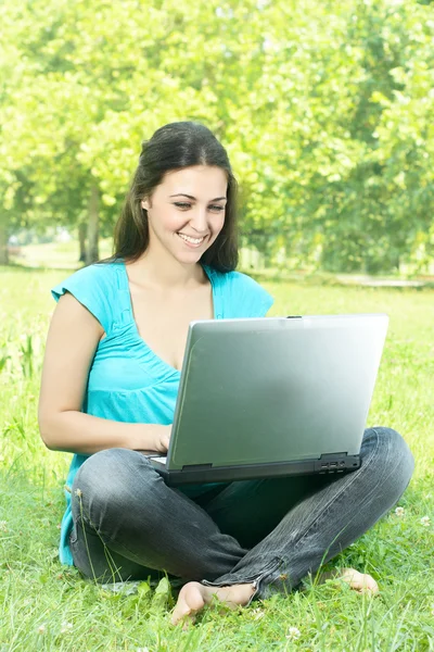 Портрет милой девушки, сидящей на траве в парке с помощью ноутбука — стоковое фото