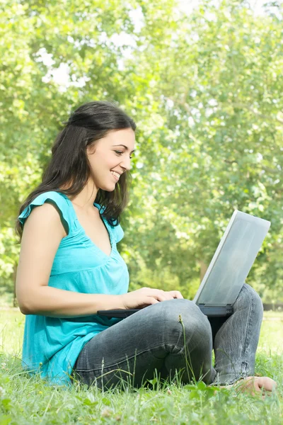 Portré egy aranyos lány ül a fűben, a parkban, használ egy laptop — Stock Fotó