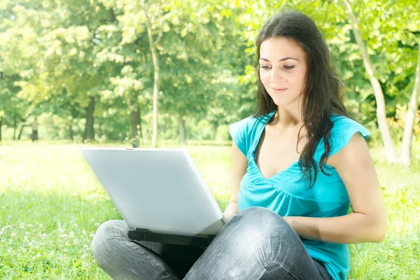 Portré egy aranyos lány ül a fűben, a parkban, használ egy laptop — Stock Fotó