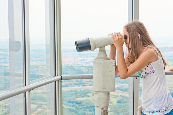 Young girl looking through tourist telescope , exploring landscape.