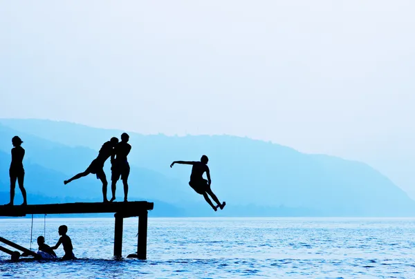 Silhouetten von Kindern, die vom Steg auf den See springen — Stockfoto