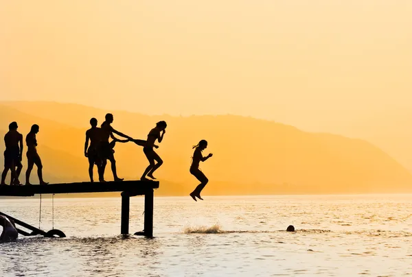 stock image Silhouettes of kids who jump off dock on the lake