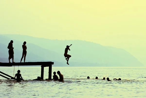 Siluetas de niños que saltan del muelle en el lago Imágenes de stock libres de derechos