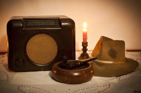 Старое радио, шляпа, труба и пепельница при свете свечей — стоковое фото