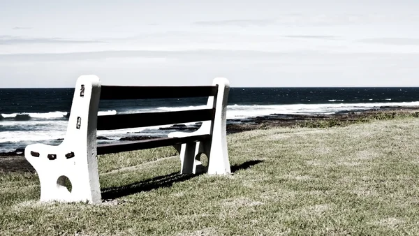 Bench on grass next to the ocean in grunge — Stock Photo, Image