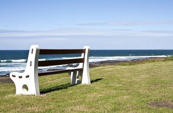 Bench on grass next to the ocean — Stock Photo, Image