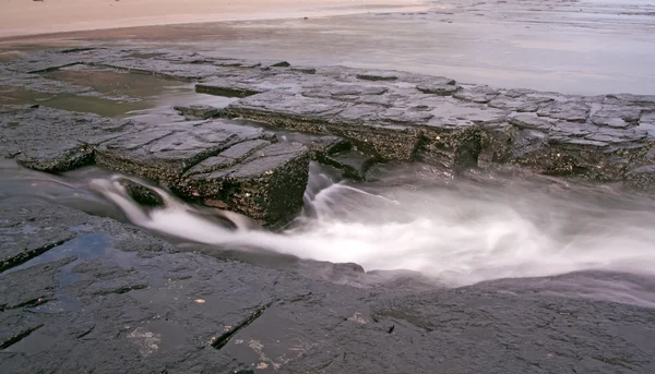 Волна отступает над скалами с размытым движением — стоковое фото