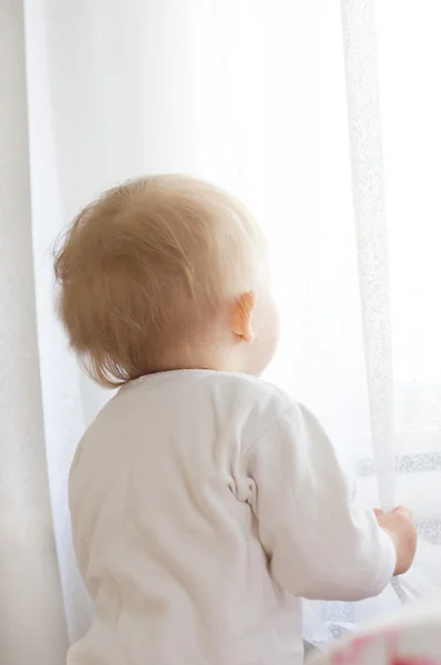 Bebê menina com suas costas olhando na janela — Fotografia de Stock