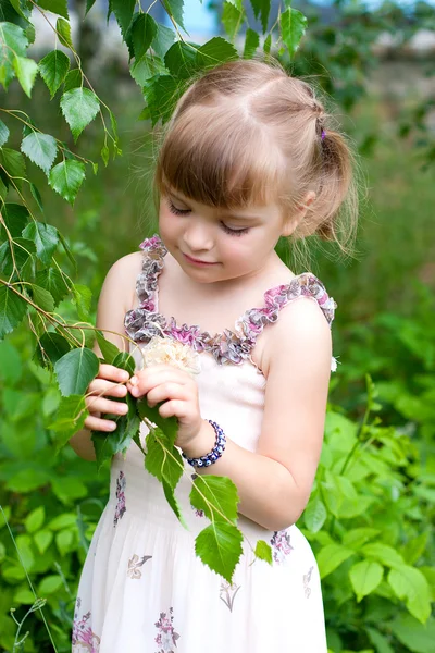 Ładny dziewczyna w parku jest biorąc pod uwagę młodych liści — Zdjęcie stockowe