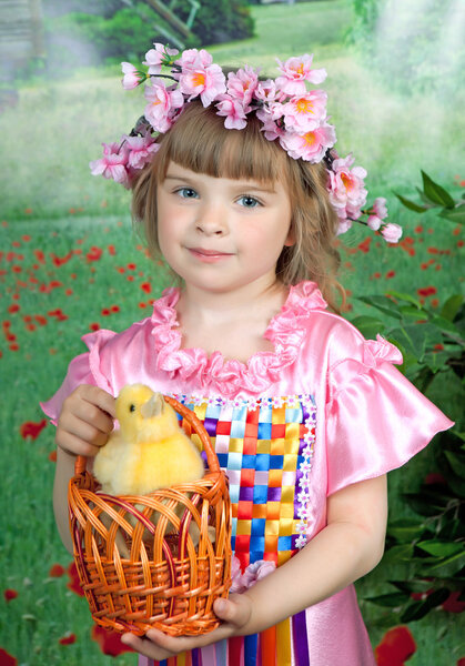 Cute girl in a pink dress and a wreath with a duckling