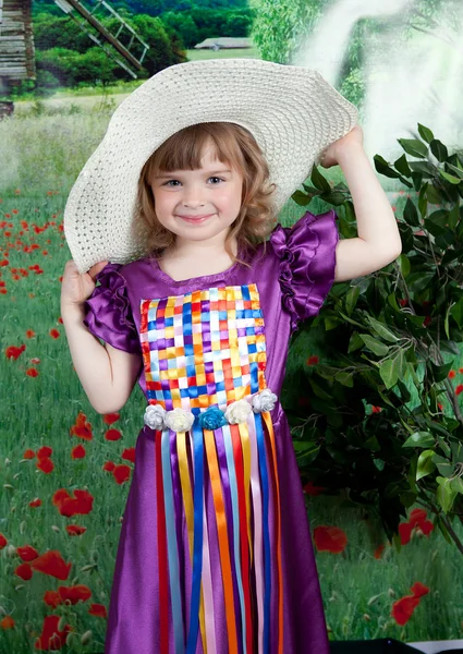 Leuk meisje in een paarse jurk en een stro hoed met bloemen — Stockfoto