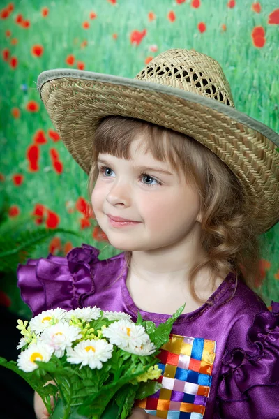 Jolie fille dans une robe violette et un chapeau de paille avec des fleurs — Photo