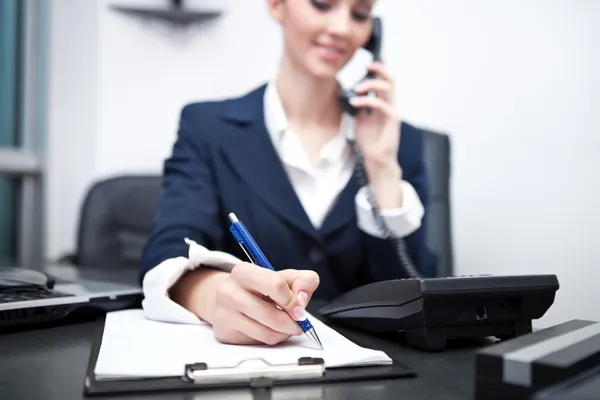 Empresária escrevendo uma consulta e usando o telefone — Fotografia de Stock