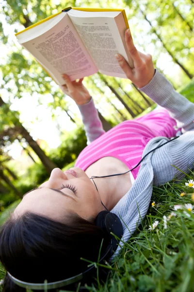Chica leyendo un libro y escuchando música en el parque — Foto de Stock