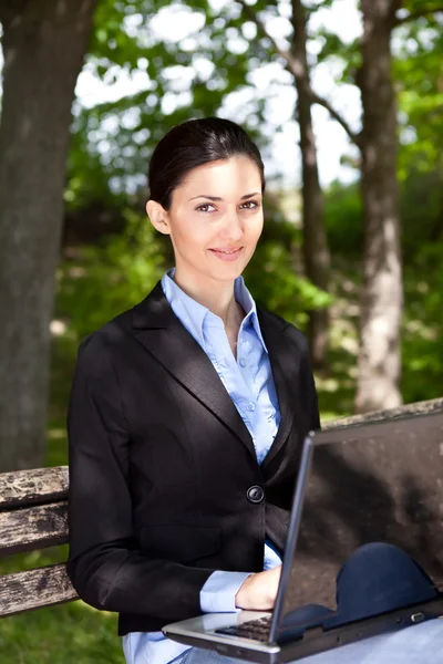 Donna con computer portatile sulla panchina in un parco — Foto Stock