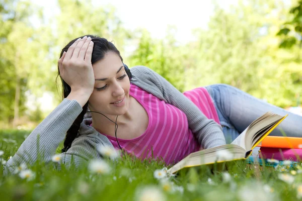 Kobieta słuchania muzyki i czytaniu książki w parku — Zdjęcie stockowe