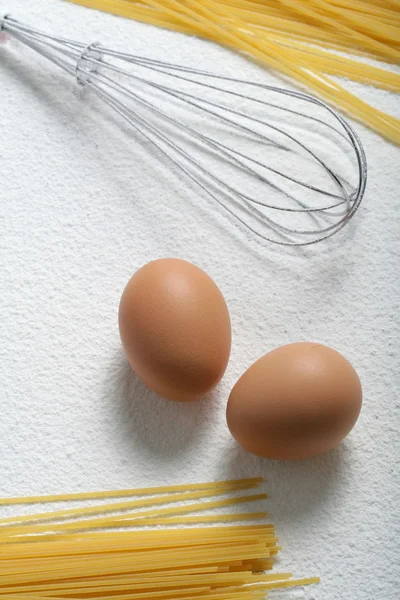 Uncooked macaroni, whisk and eggs — Stock Photo, Image