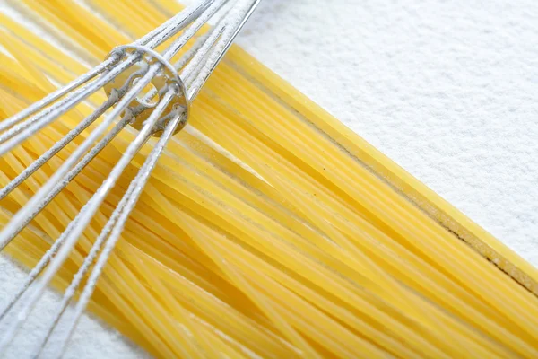 Wire whisk and spaghetti on flour — Stock Photo, Image