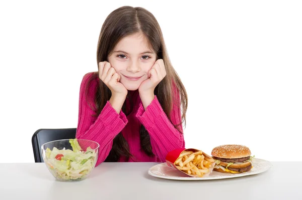 Маленькая девочка со здоровой и нездоровой пищей — стоковое фото